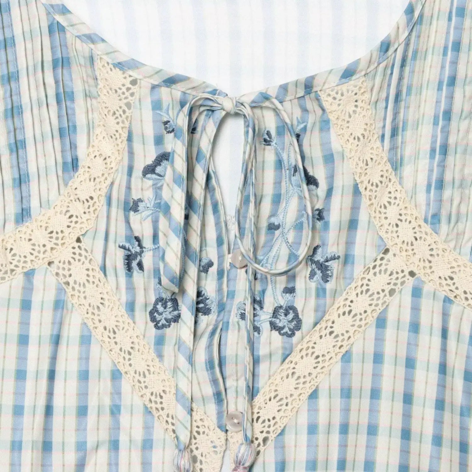 Vertical shot of partial front button placket, round shell buttons surrounded by vintage flower embroidery and lace panels