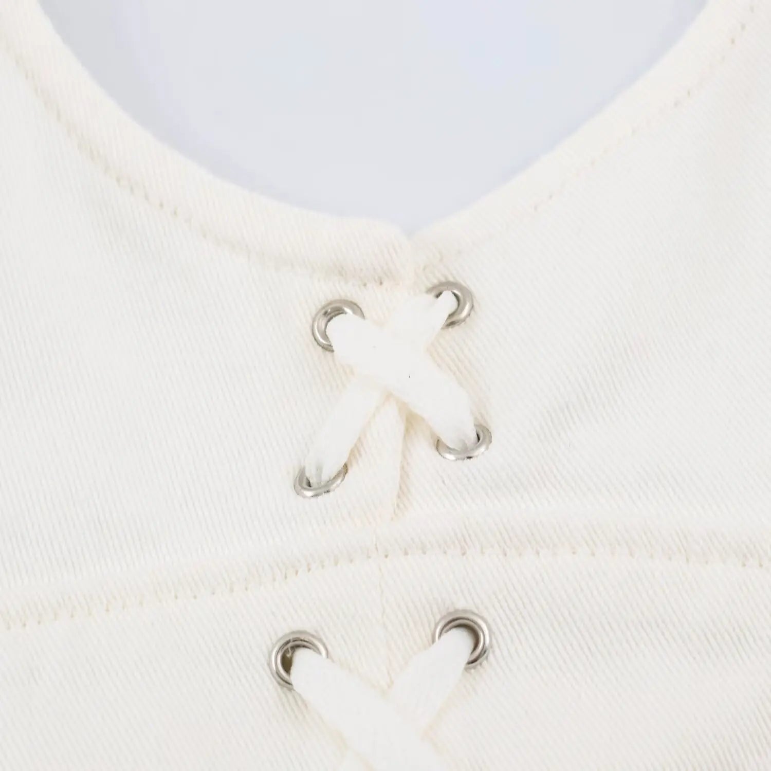 Detailed close up of front cross lace up with silver metal eyelets on white twill mini dress