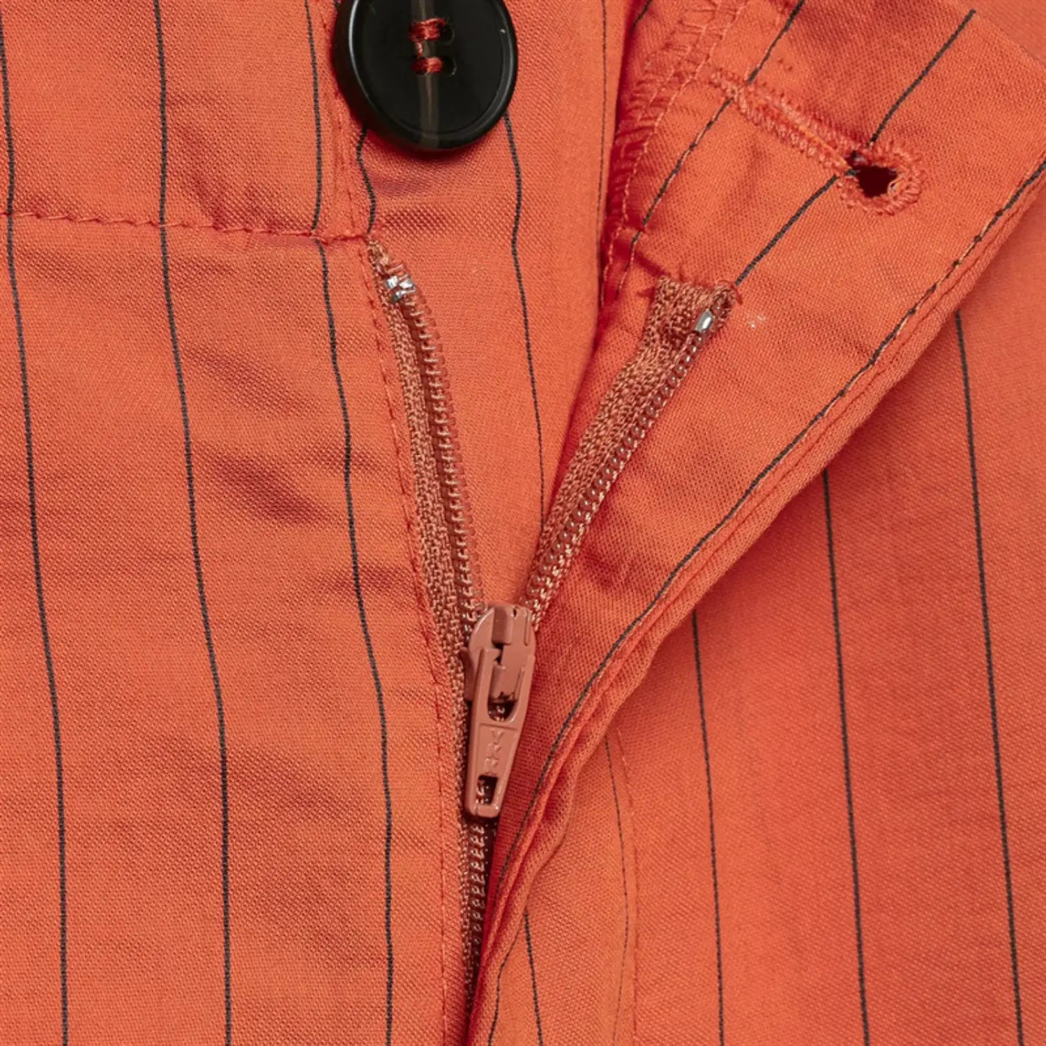 Extreme macro shot of fly hardware, matching orange zipper tape, round dark button, neat reinforced buttonhole stitching