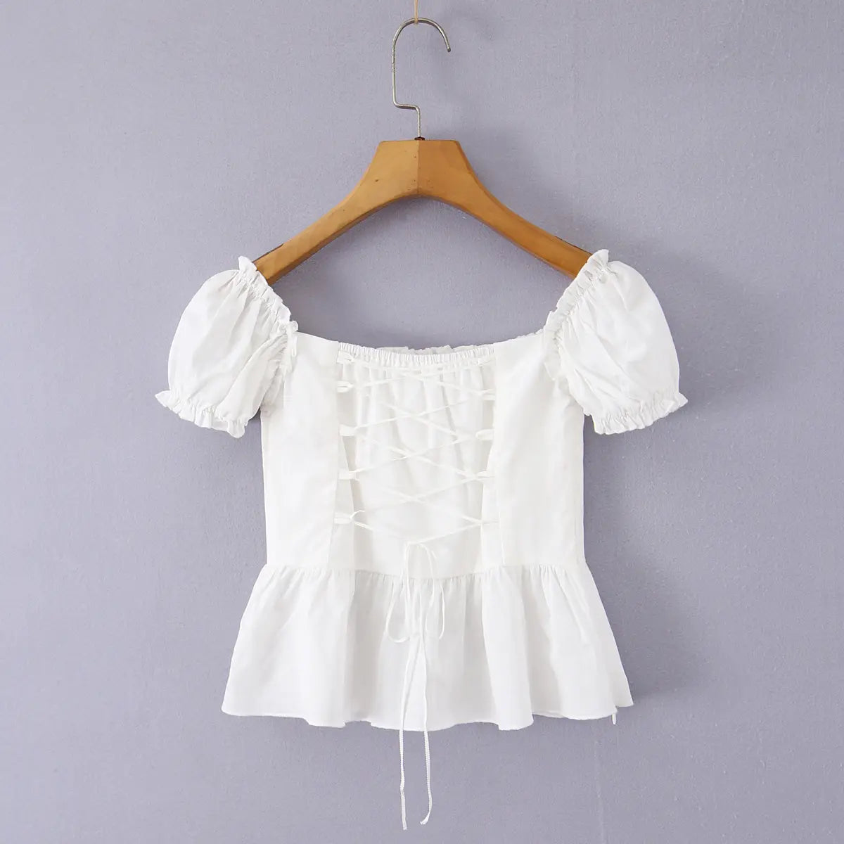 Full back view of a white off-shoulder peplum top, highlighting the lace-up detail, puff sleeves, and flared peplum hem.