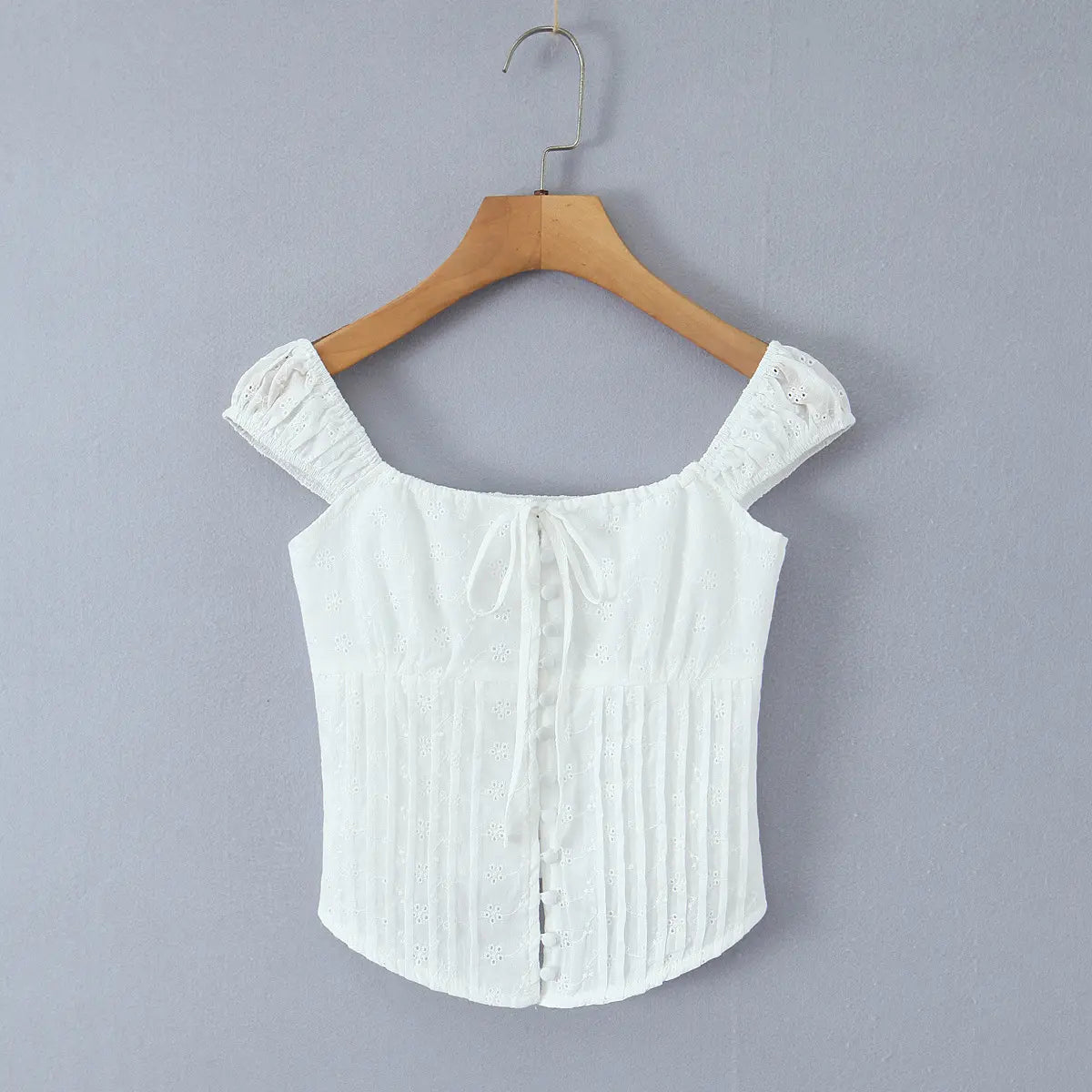 Full front view of a white eyelet embroidered bustier top on a hanger, showing the square neckline, puff sleeves, and curved corset-style hem.
