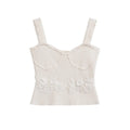 Full front view of a white ribbed cami top, featuring bustier-style seams, scalloped straps, and a floral lace waistband.