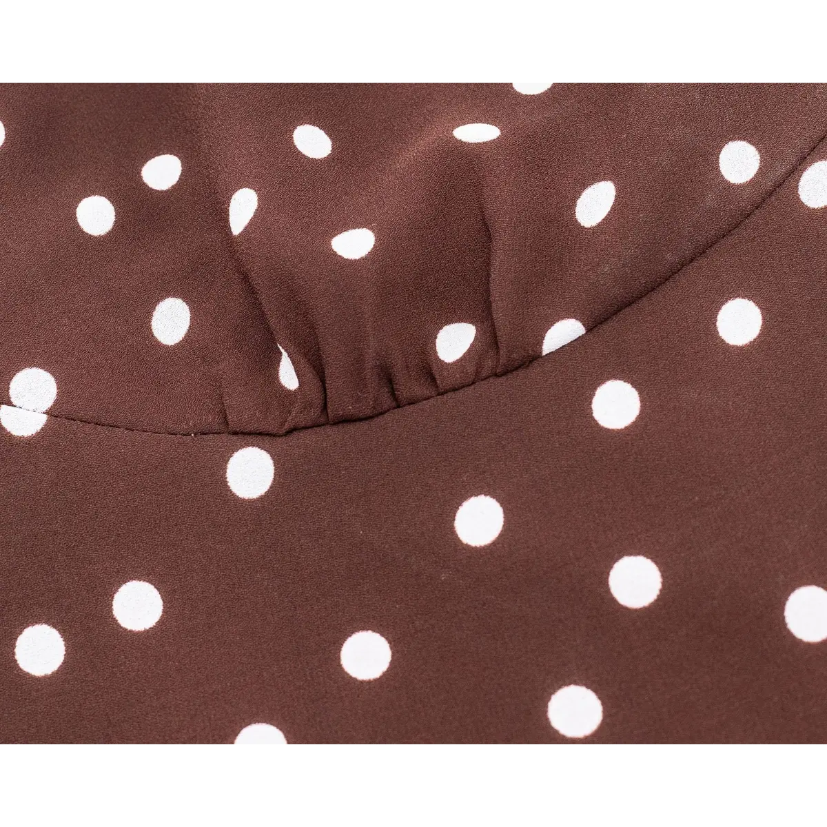 Close-up of the gathered bust on a brown and white polka dot dress, highlighting the V-neck construction and smooth fabric texture.