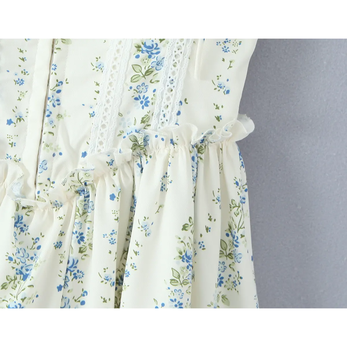  Close-up of the gathered waist and eyelet lace panels on a cream floral dress, highlighting the construction.