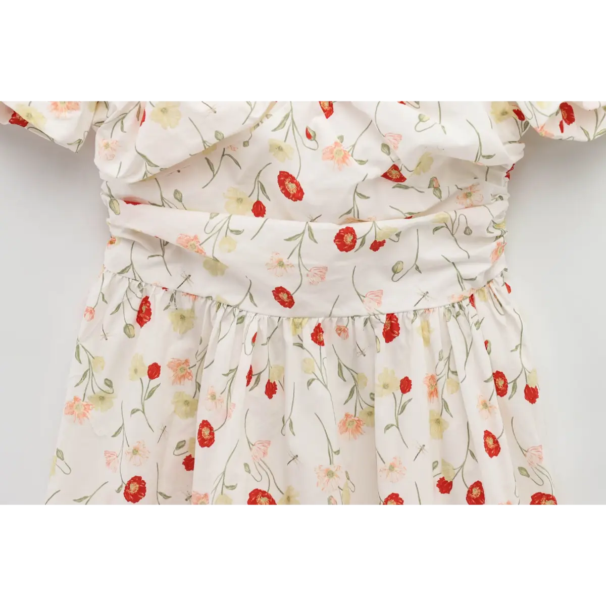 Close-up of the gathered waist on a white poppy-print dress, showing the ruched fabric and floral pattern.