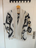 Geometric diamond intarsia open front cardigan hanging on door, front view