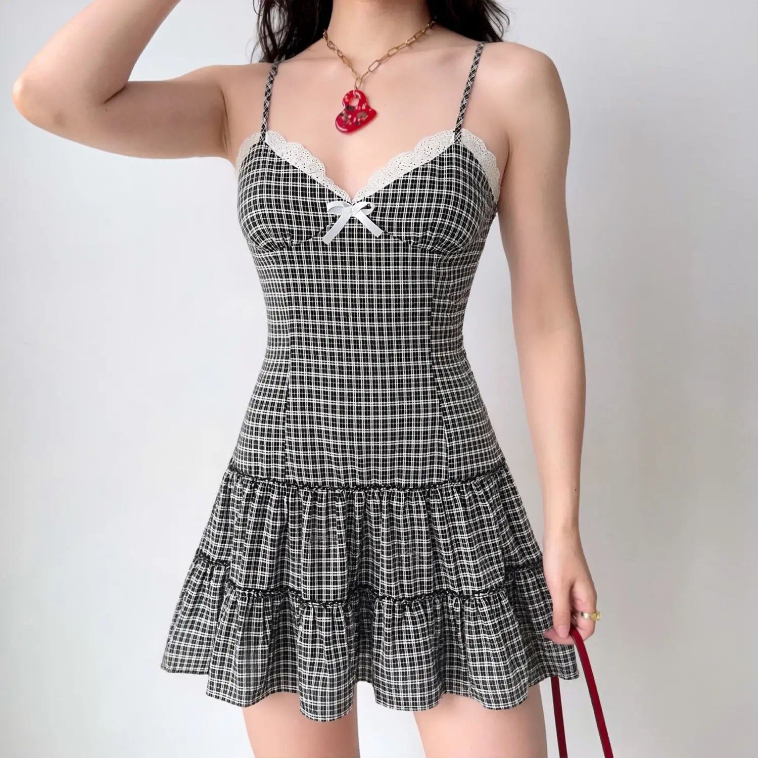 Female model wearing black white gingham cami mini dress, v‑neck lace trim with front bow, tiered ruffle short skirt