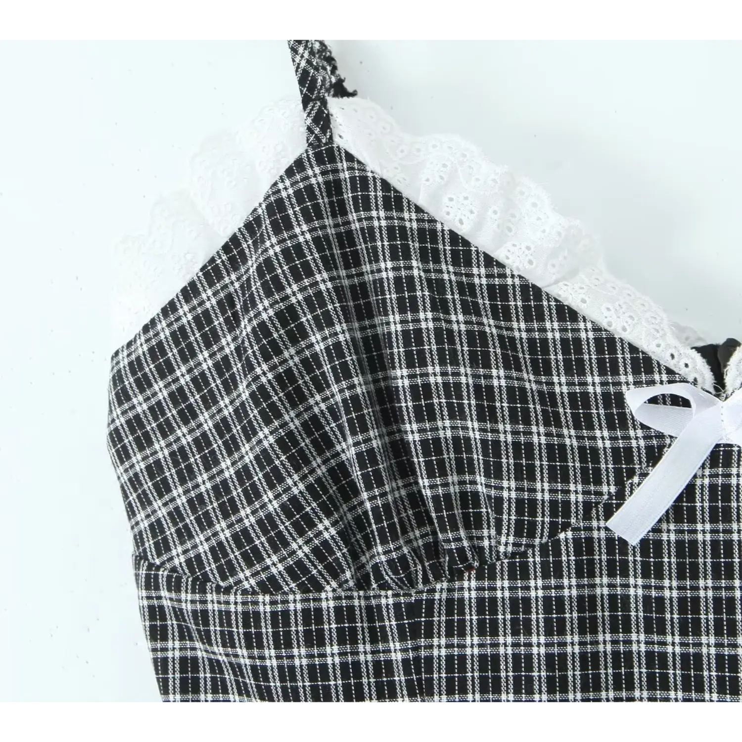 Fabric close‑up, white scalloped eyelet lace trim at v‑neckline, black and white gingham woven texture, front ribbon bow detail