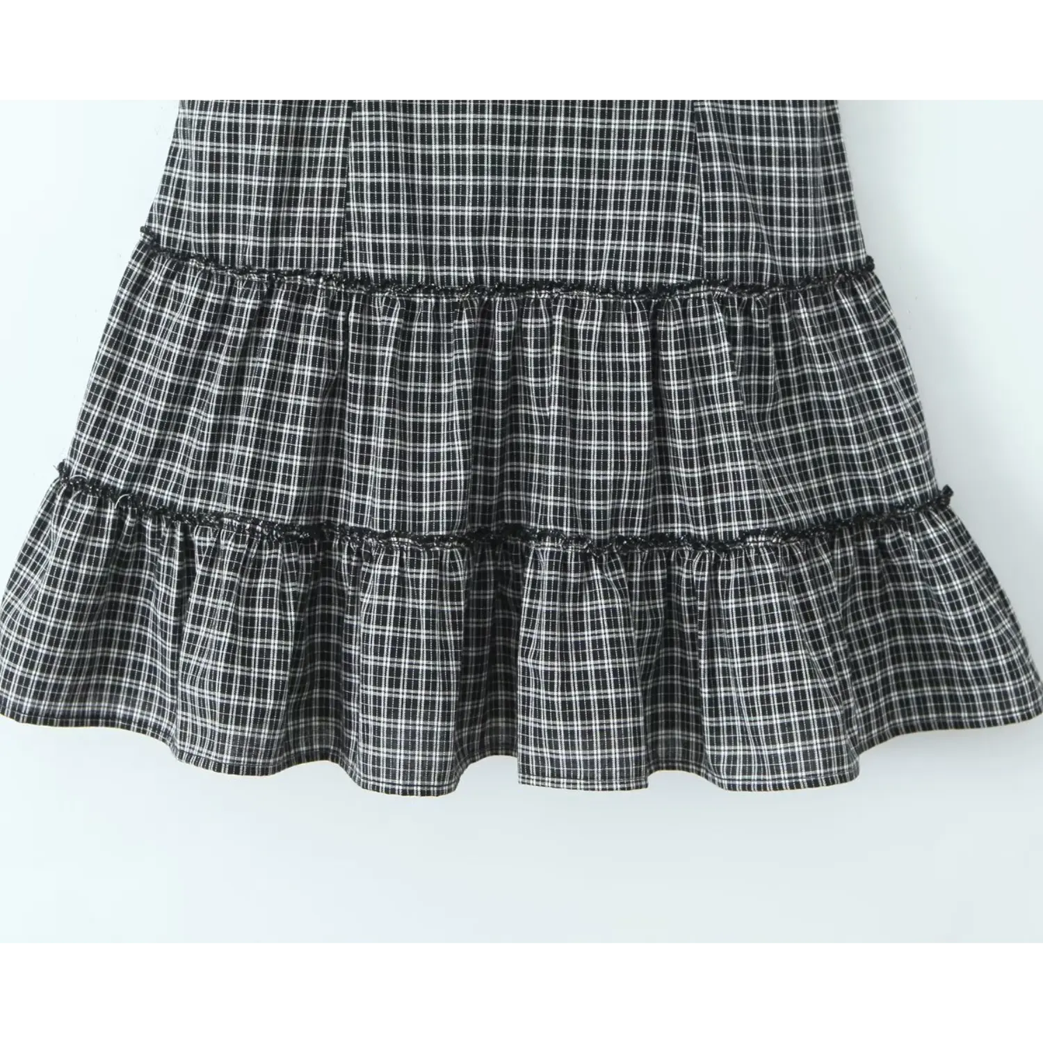 Close‑up tiered ruffle skirt hem of gingham cami dress, layered ruffle panels with black picot edge trim
