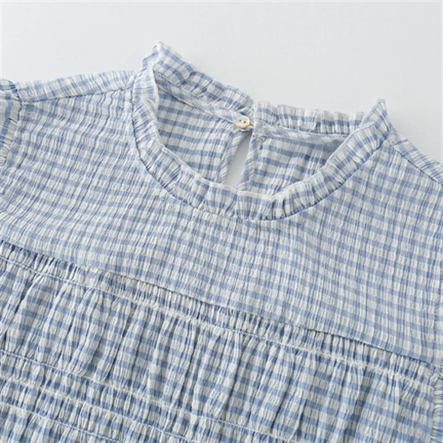 Macro closeup back ruffle neck keyhole, single matching fabric button, neat folded binding stitching, crinkle light blue gingham material