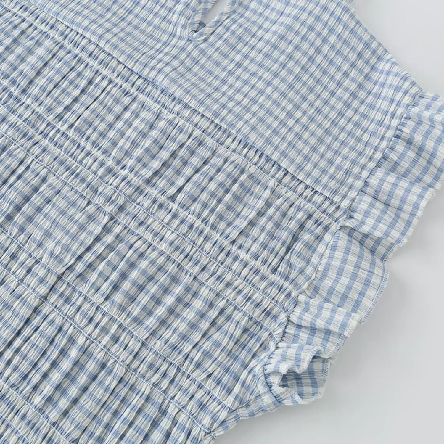 Shoulder flutter cap sleeve detail, double layer ruffle edge, continuous horizontal smock stitching across bust, crinkle gingham fabric