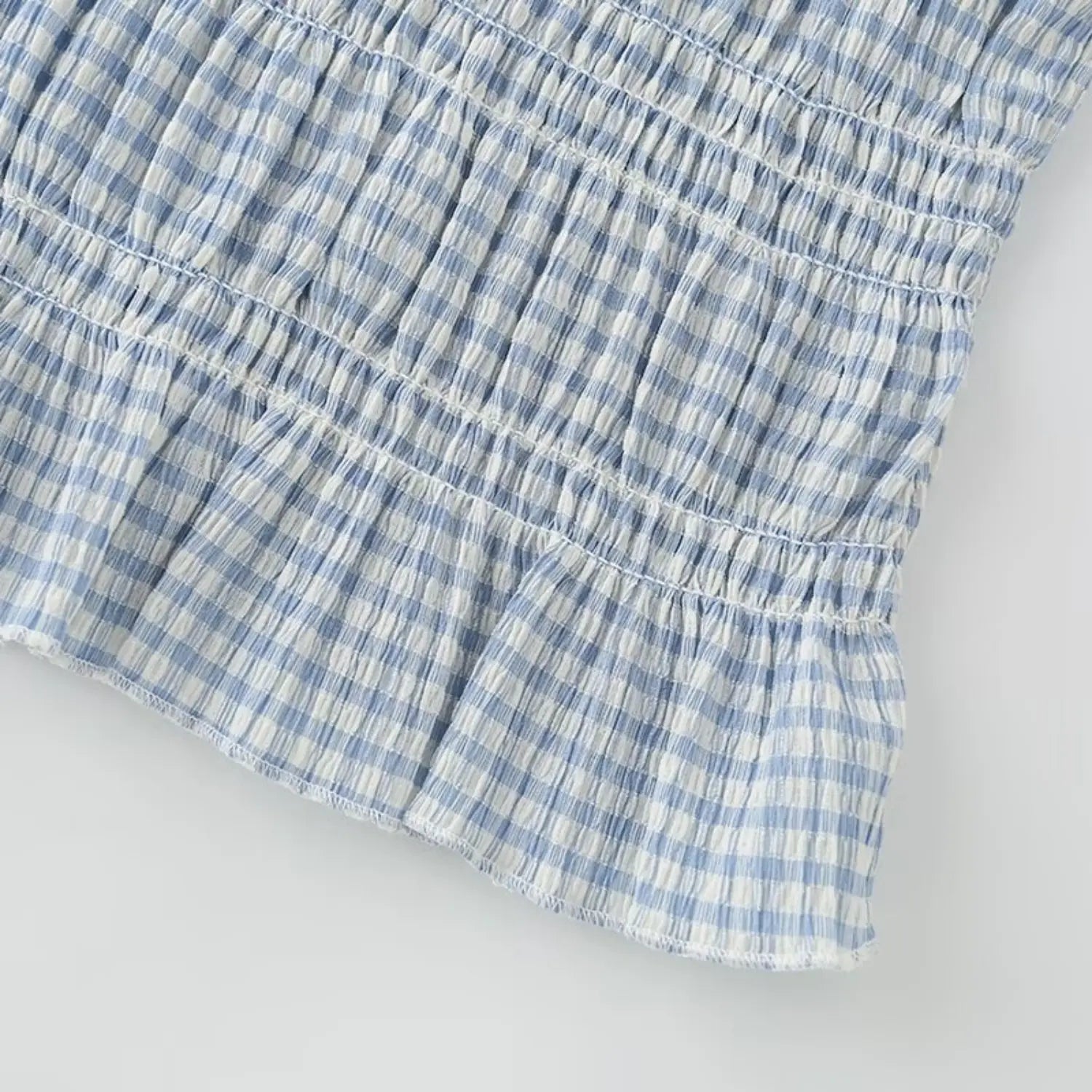 Waist section macro shot light blue mini gingham fabric, dense horizontal stretch shirring, natural crinkle lightweight woven texture