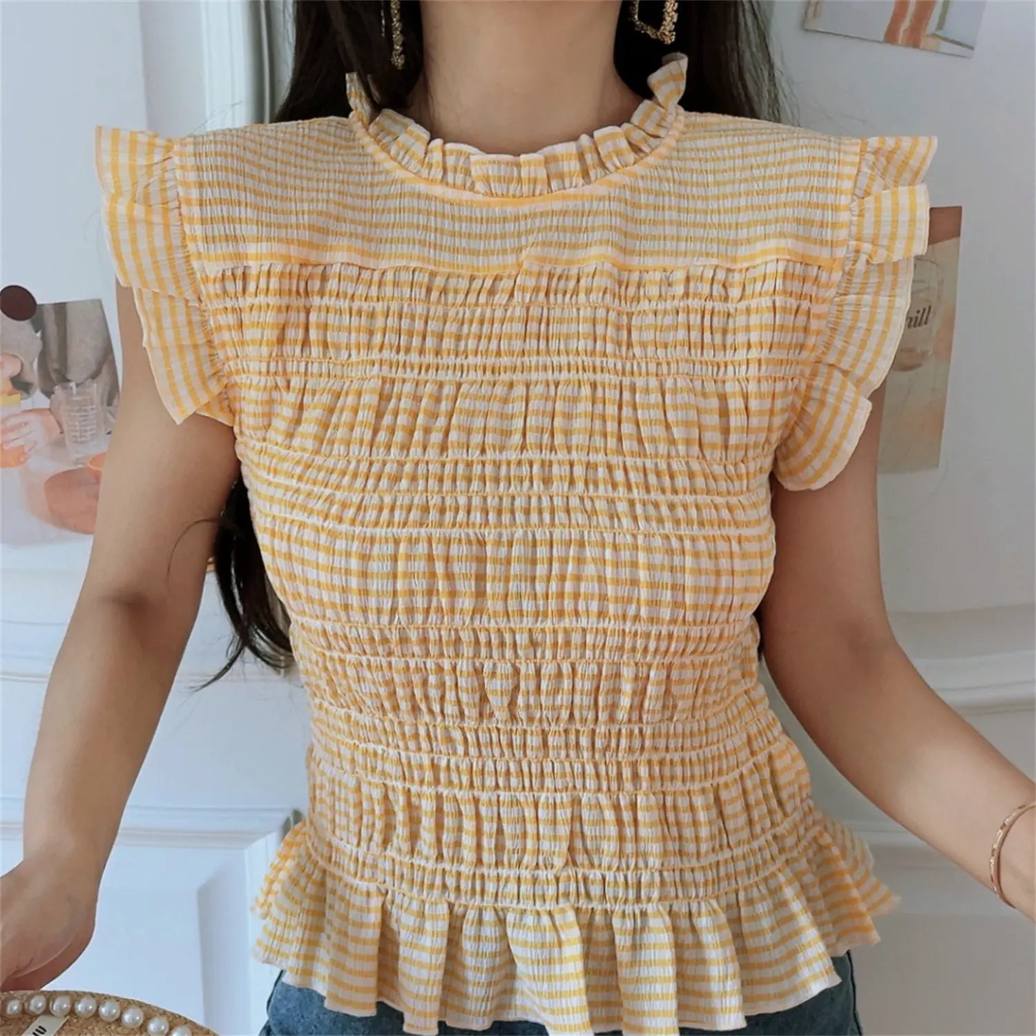 Lifestyle model shot yellow gingham smocked sleeveless top, frilled mock neck, ruffle wing cap sleeves, all-over stretch smocked fabric, flared peplum hem, casual summer daily outfit