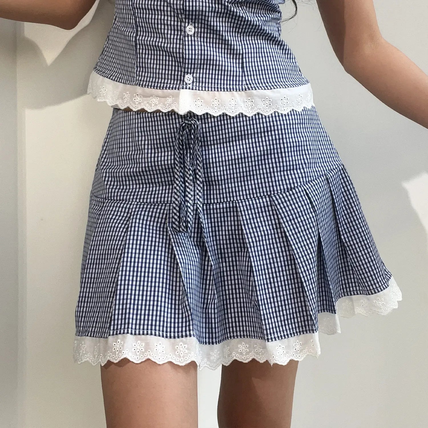 Gingham two piece set model lower body lifestyle shot, highlight high waist pleated skirt waist drawstring hem lace trim match cropped top full schoolgirl feminine daily outfit shot