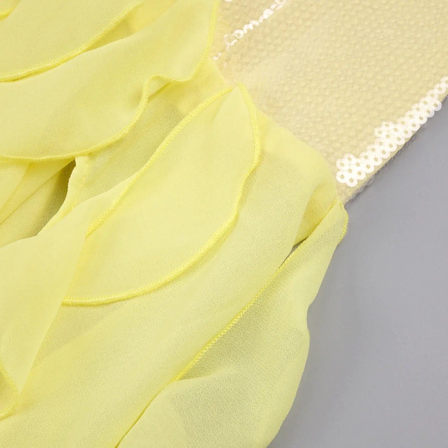 Close-up stitching detail of yellow gown transition area, textured sequin bust fabric connected with layered sheer chiffon ruffle hem