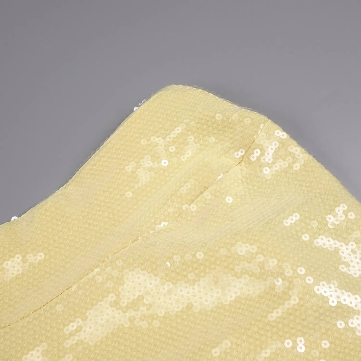Partial close-up of stitched seam on yellow sequin stretch mesh bodice, dense scattered reflective sequins with neat finished fabric edge