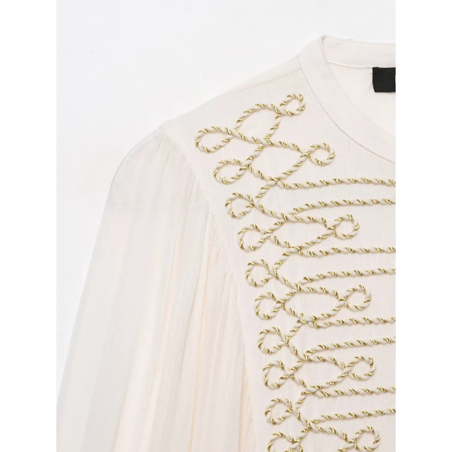 Close‑up detail of gold cord decorative embroidery on shoulder of white women blouse, textured fabric
