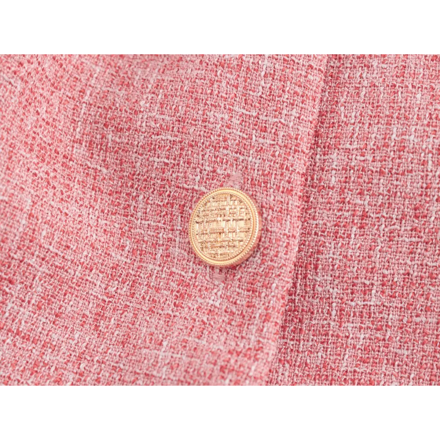 Close-up round gold metal button, woven tweed emboss pattern on surface, matching pink tweed front placket