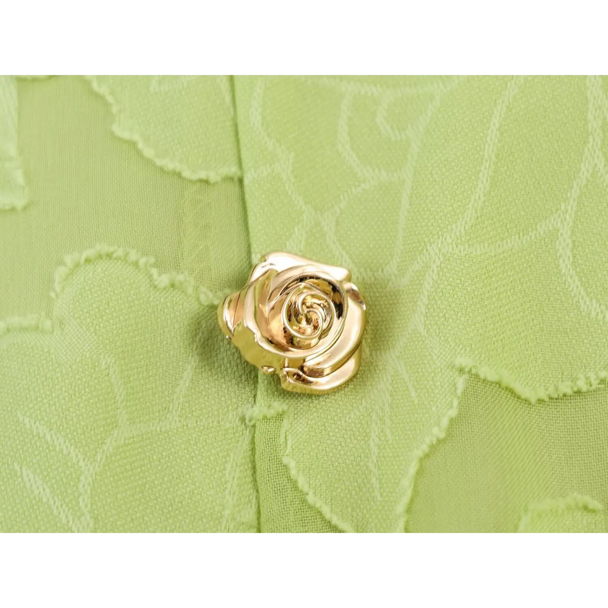 Macro close-up of 3D gold rose decorative button on light green jacquard maxi dress