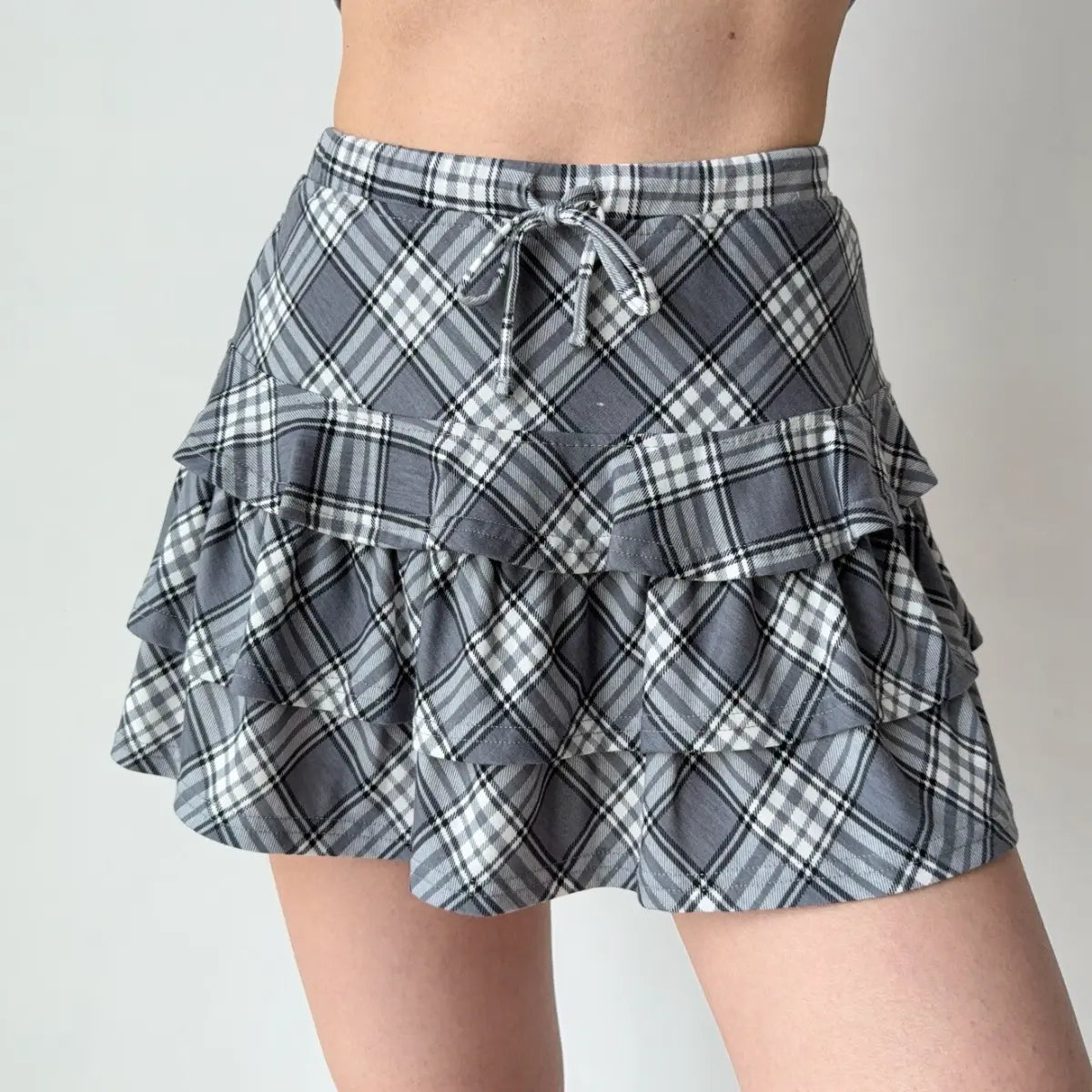 Front view of the gray plaid tiered ruffle mini skirt with a drawstring waist.