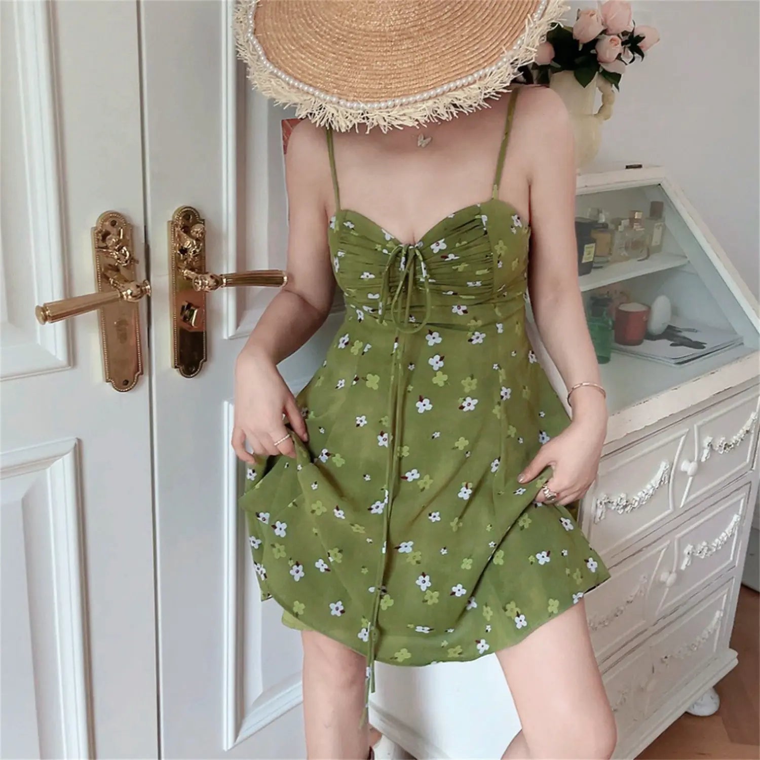 Avocado green tiny floral fitted cami mini dress full front model shot, v-neck drawstring bust adjustable thin straps, full body display against white cabinet decor background