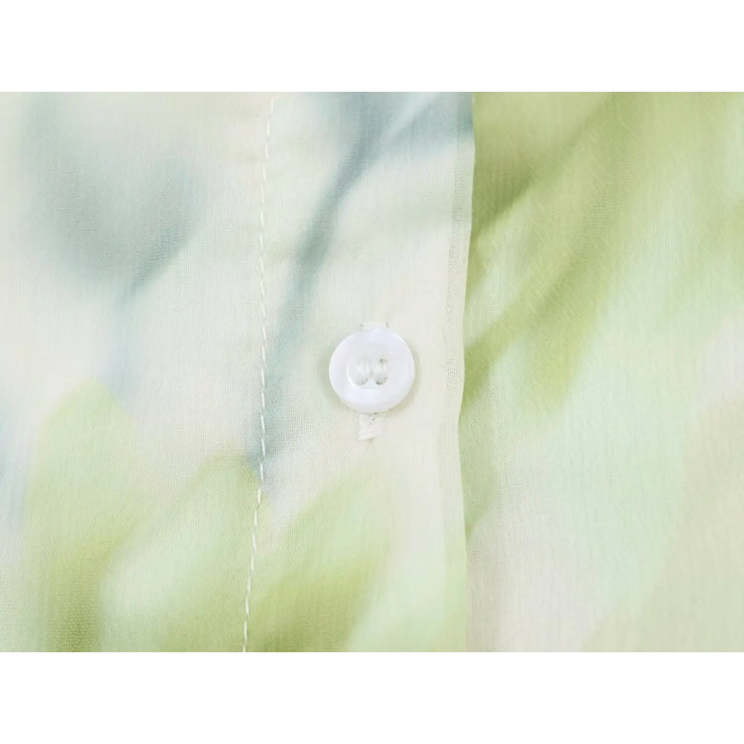 Close‑up of round white front button on green floral print chiffon maxi dress, stitching detail