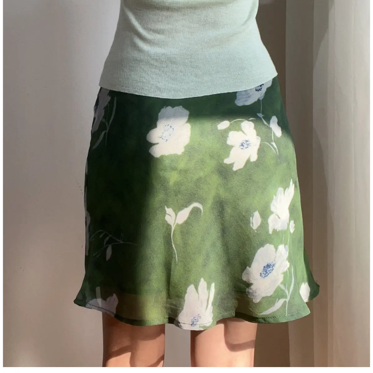 Woman wearing a green floral chiffon mini skirt with white flowers, paired with a light green top, showing the skirt's flowy silhouette.