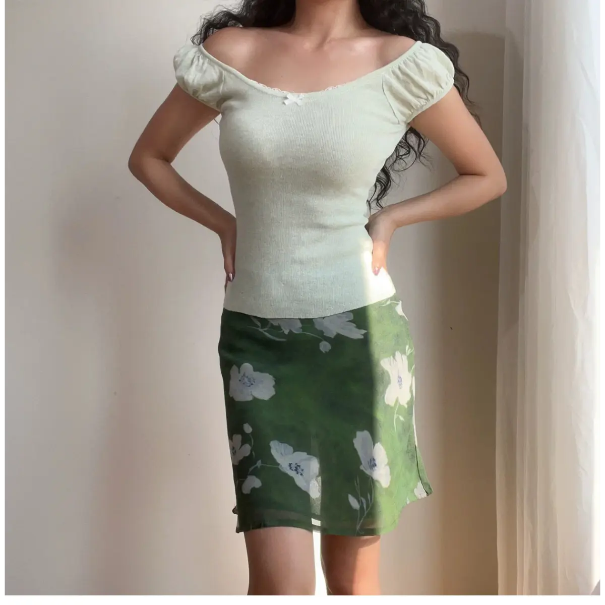  Full-body view of a woman wearing a green floral chiffon mini skirt with white flowers, paired with a light green off-the-shoulder top.