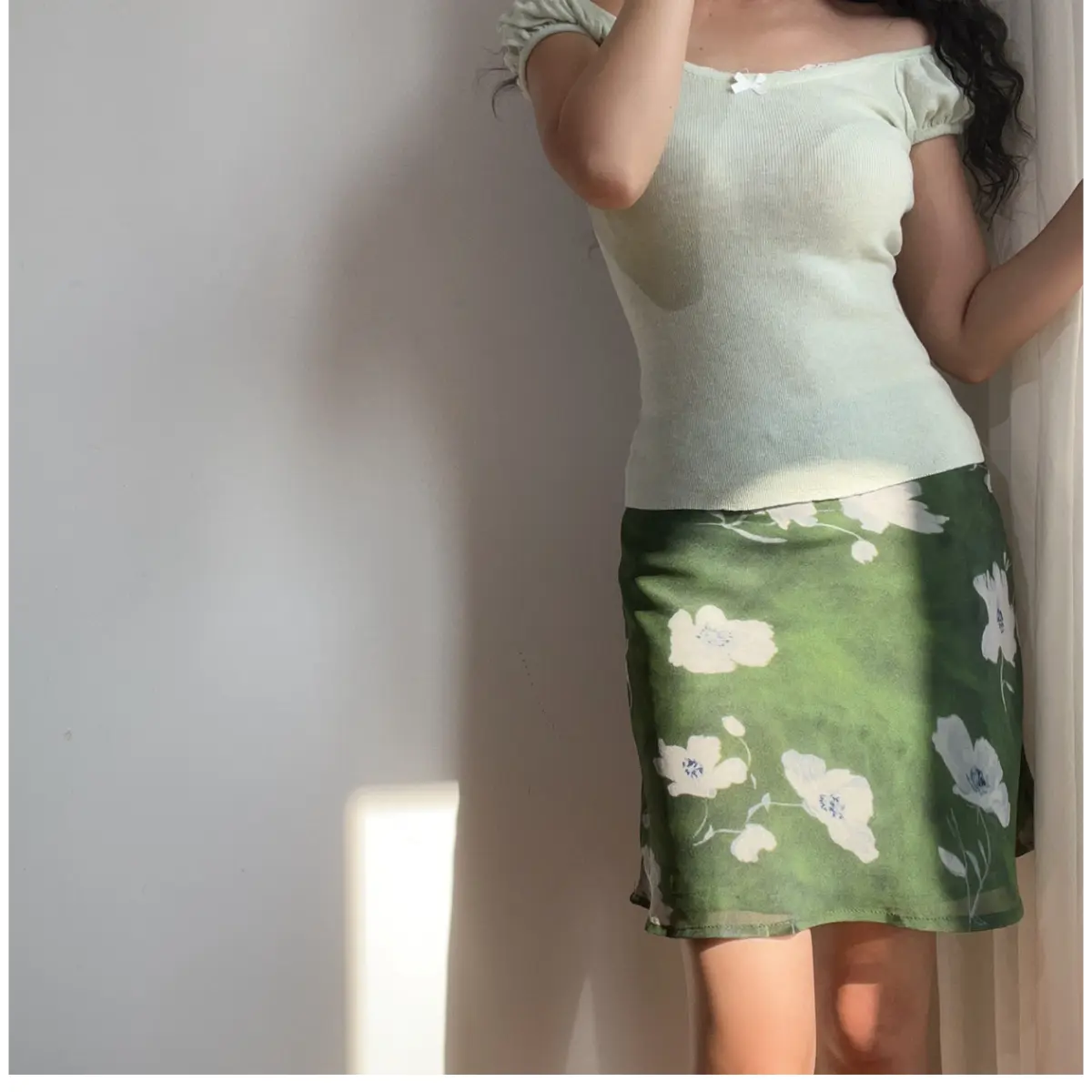 Side view of a green floral chiffon mini skirt with white flowers, paired with a light green off-the-shoulder top, showing the skirt's length and drape.