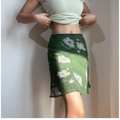 Close-up view of the waistband of a green floral chiffon mini skirt with white flowers, showing the delicate lace trim and bow detail.