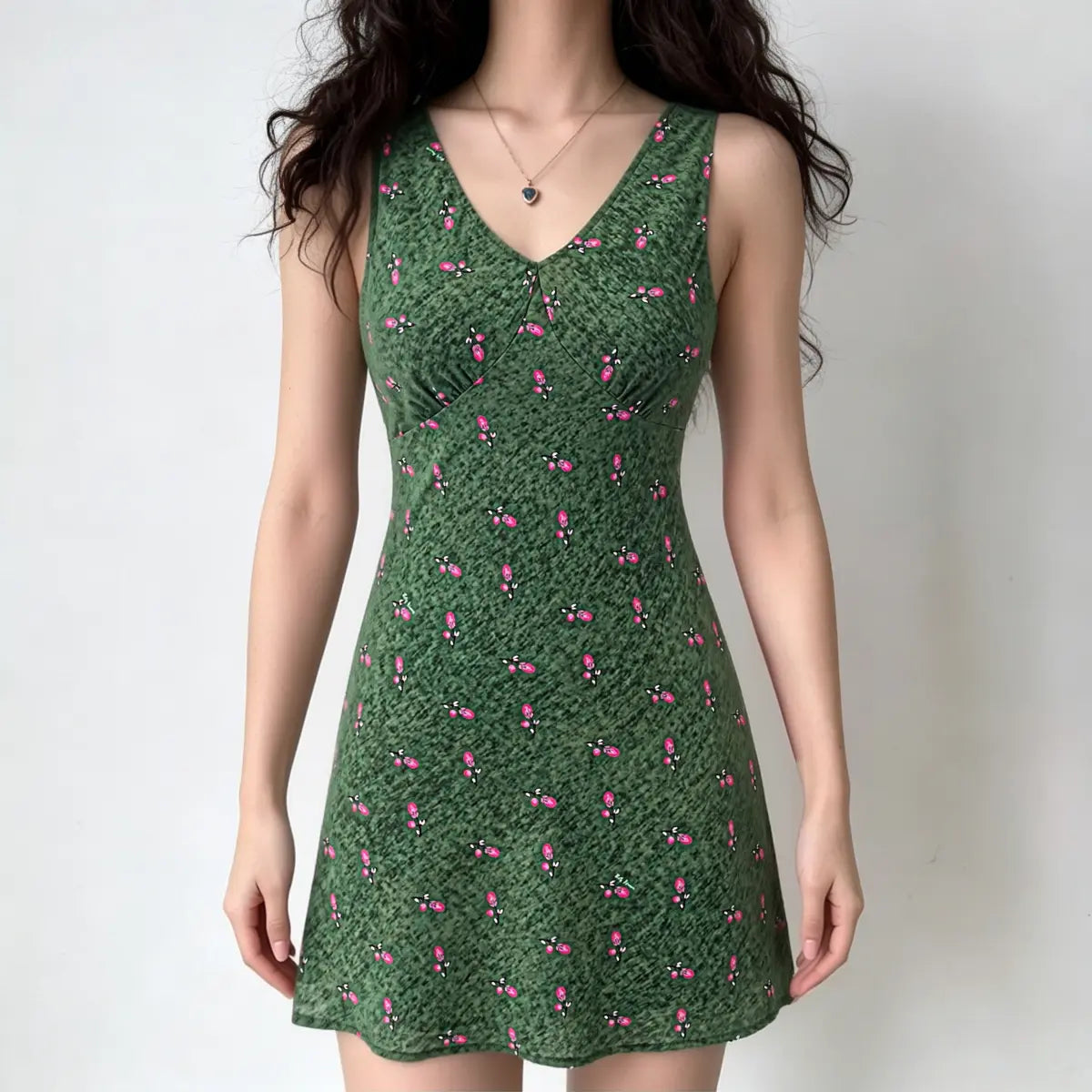 Full-body shot of a woman wearing a green floral print sleeveless V-neck mini dress.