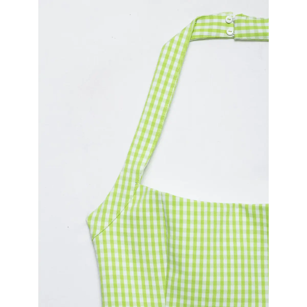Close-up of the halter neckline buttons on a green gingham dress, showing the closure mechanism.