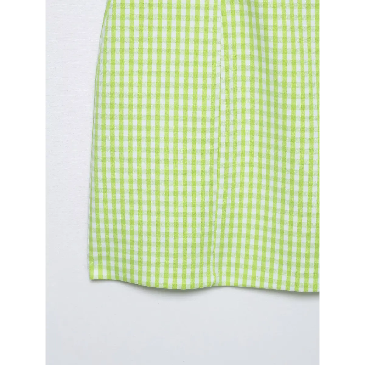 Close-up of the bottom hem seam on a green gingham halter dress, showing the stitching and fabric finish.
