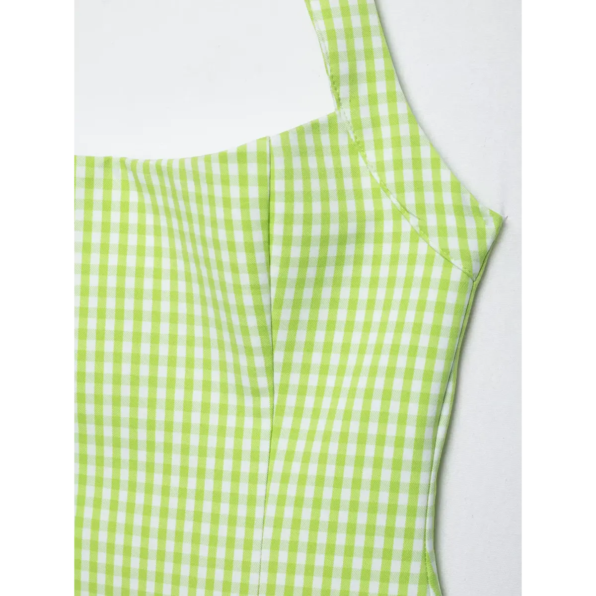 Close-up of the side seam and bust area of a green gingham halter dress, showing the tailored construction.