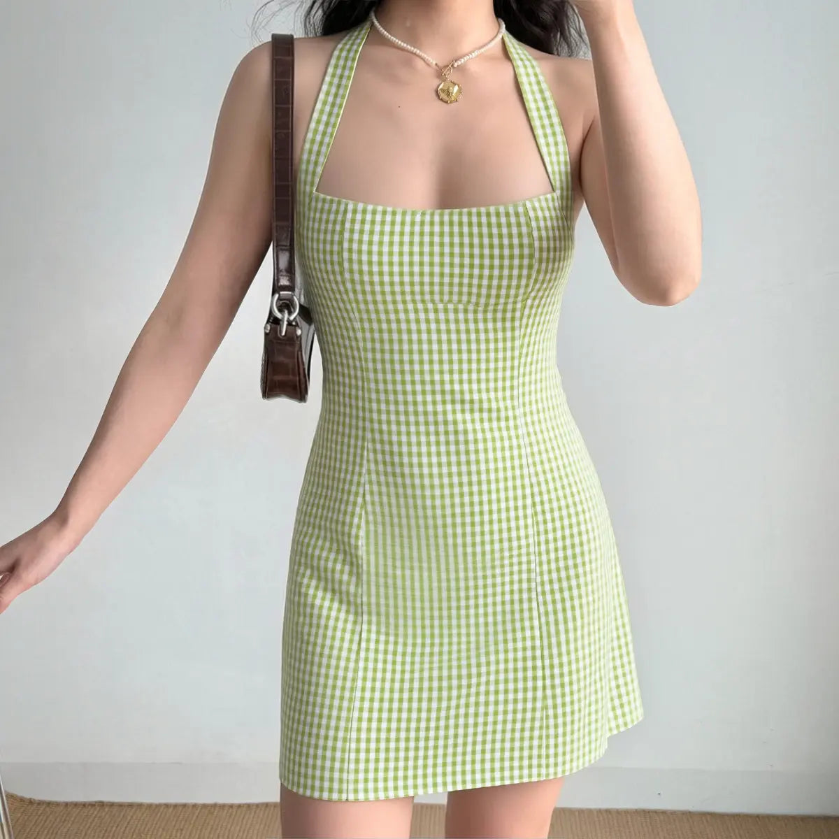 Model wearing a green and white gingham halter mini dress, showing the fitted silhouette, halter neckline, and casual styling.