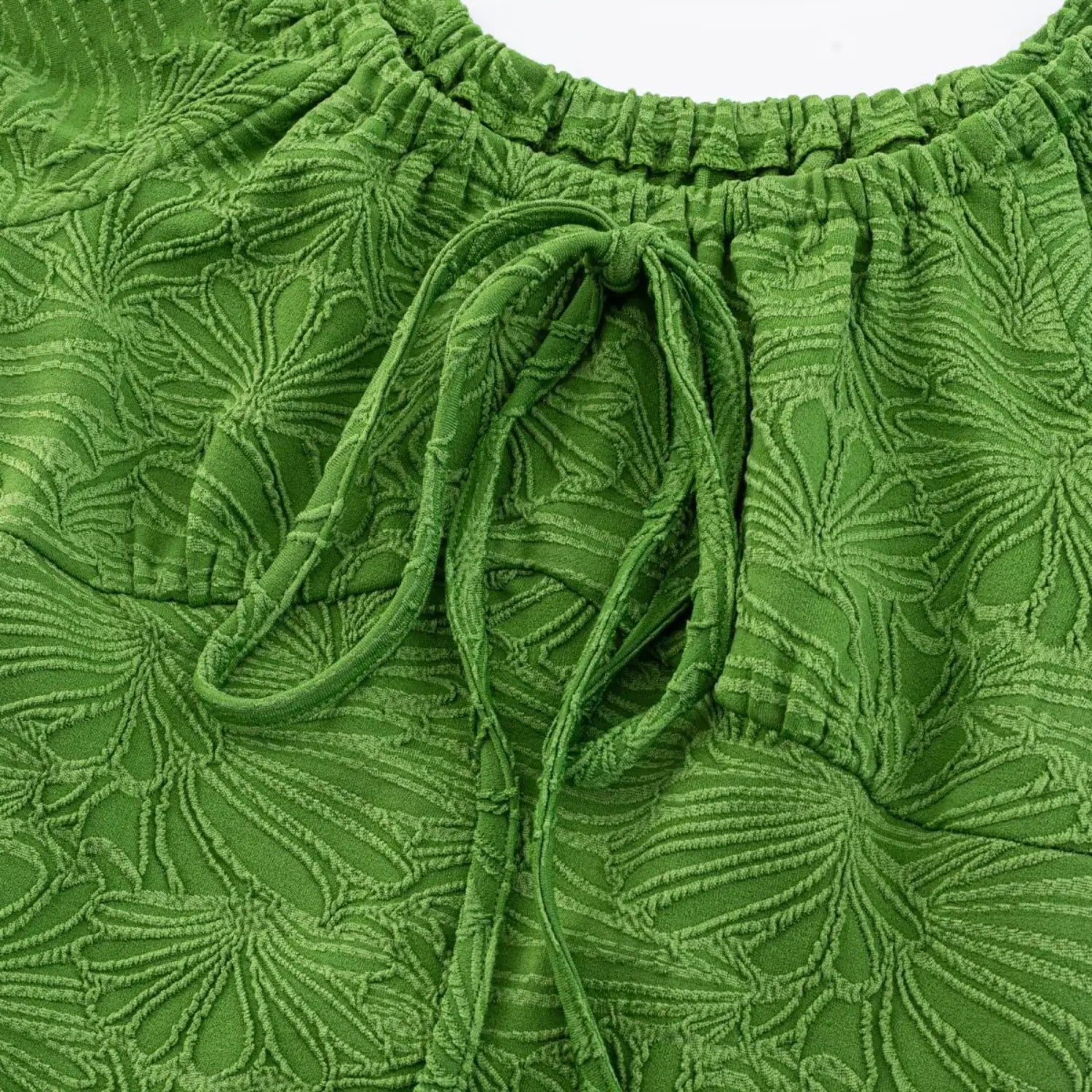 Macro close flat shot of center bust drawstring tie bow on vibrant green leaf embossed knit fabric, elastic gathered neck surrounding detail