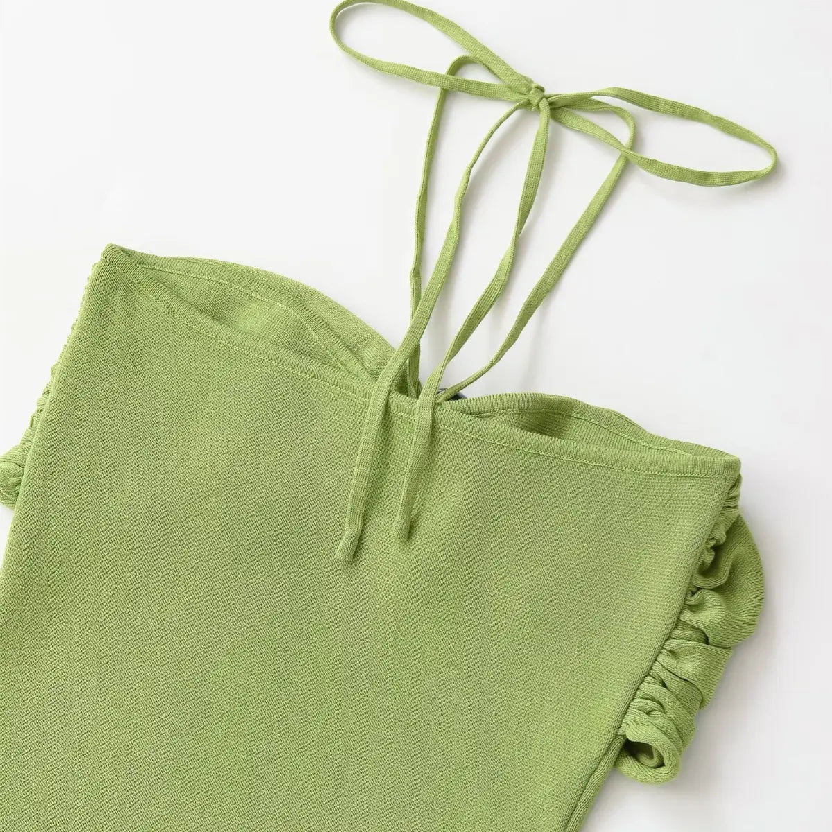 Close-up of the halter neck tie on green knit dress, showing straps and central decorative bead.