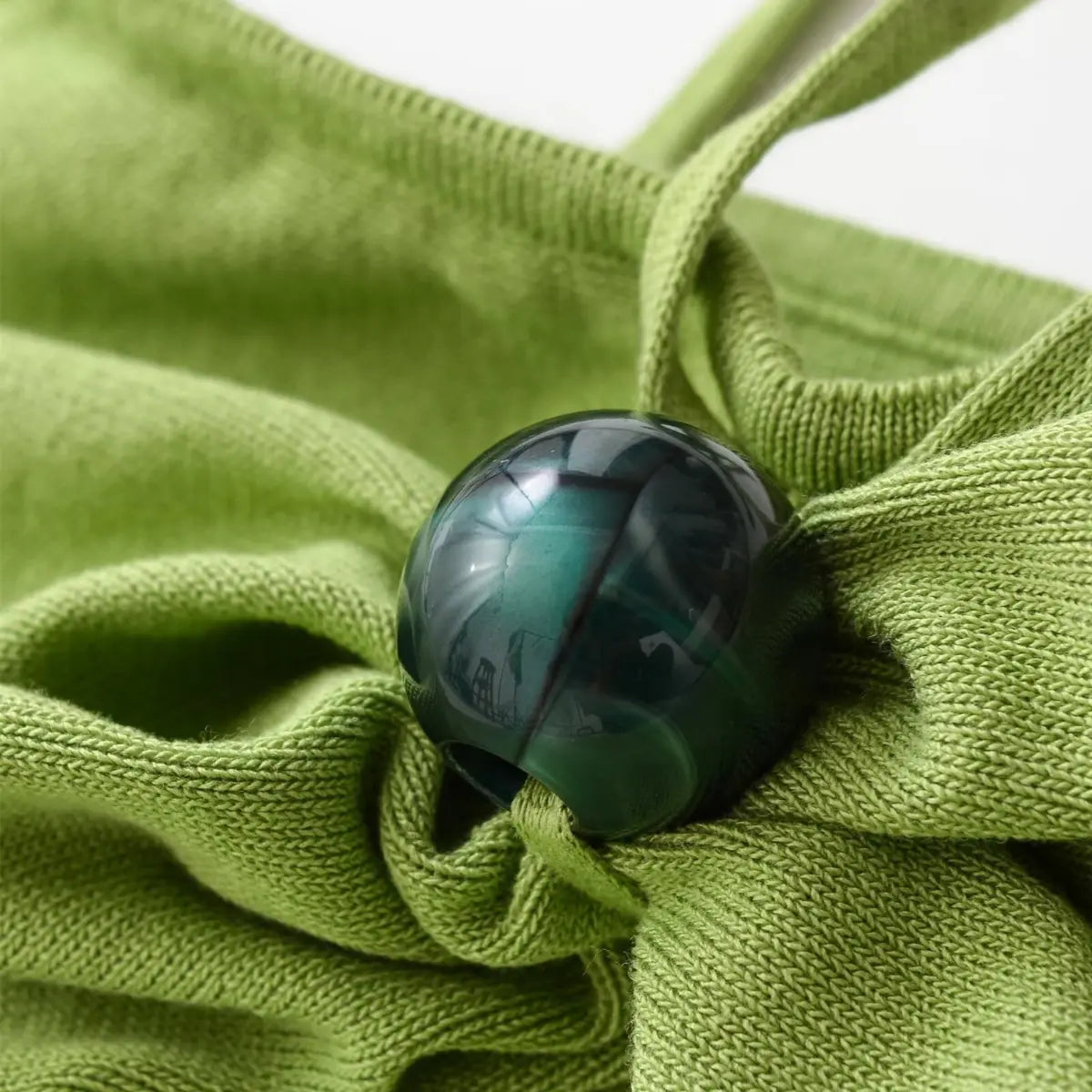 Close-up of the central decorative bead on green knit halter dress, showing fabric texture and gathered design.