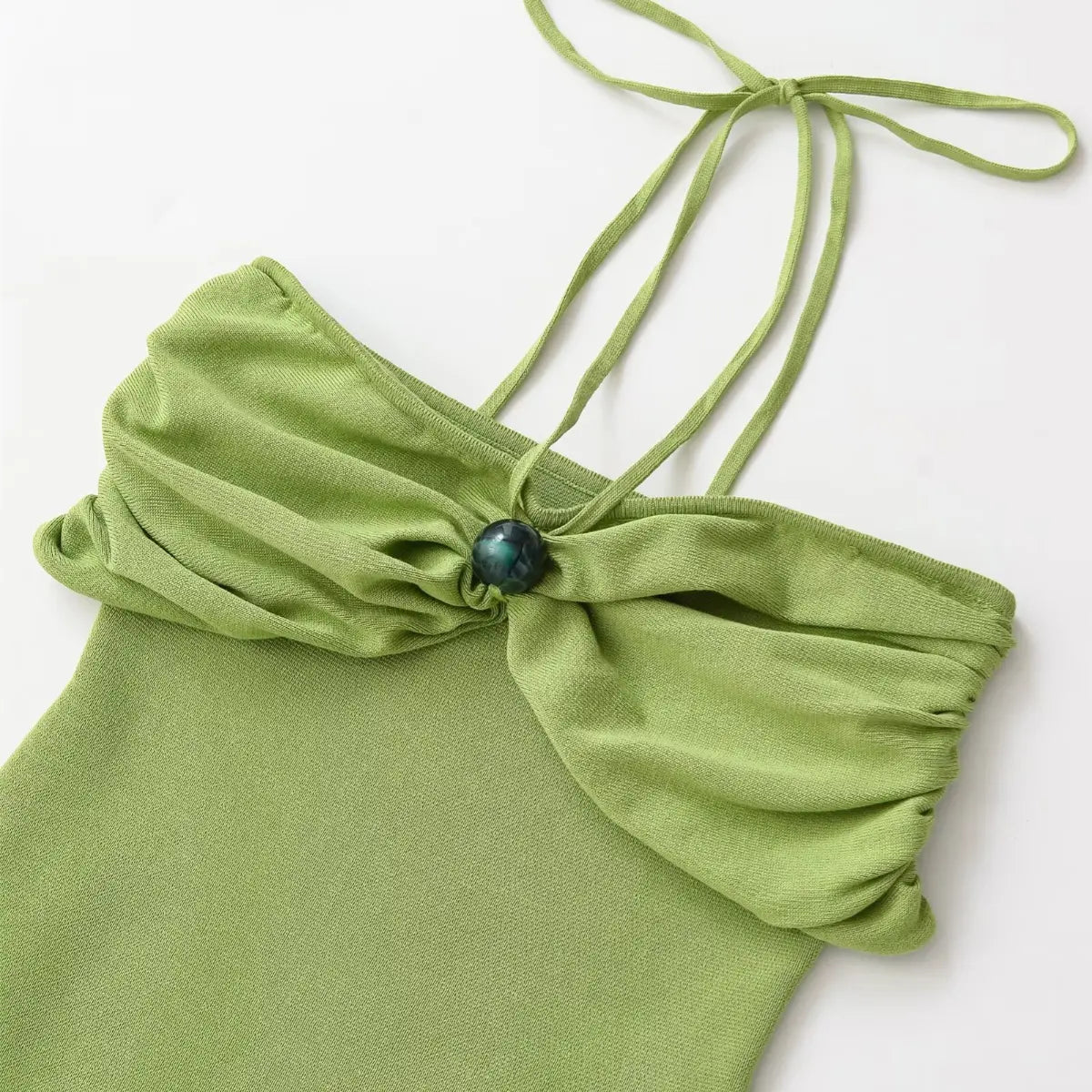 Close-up of the halter neck tie on green knit dress, showing straps and central decorative bead.