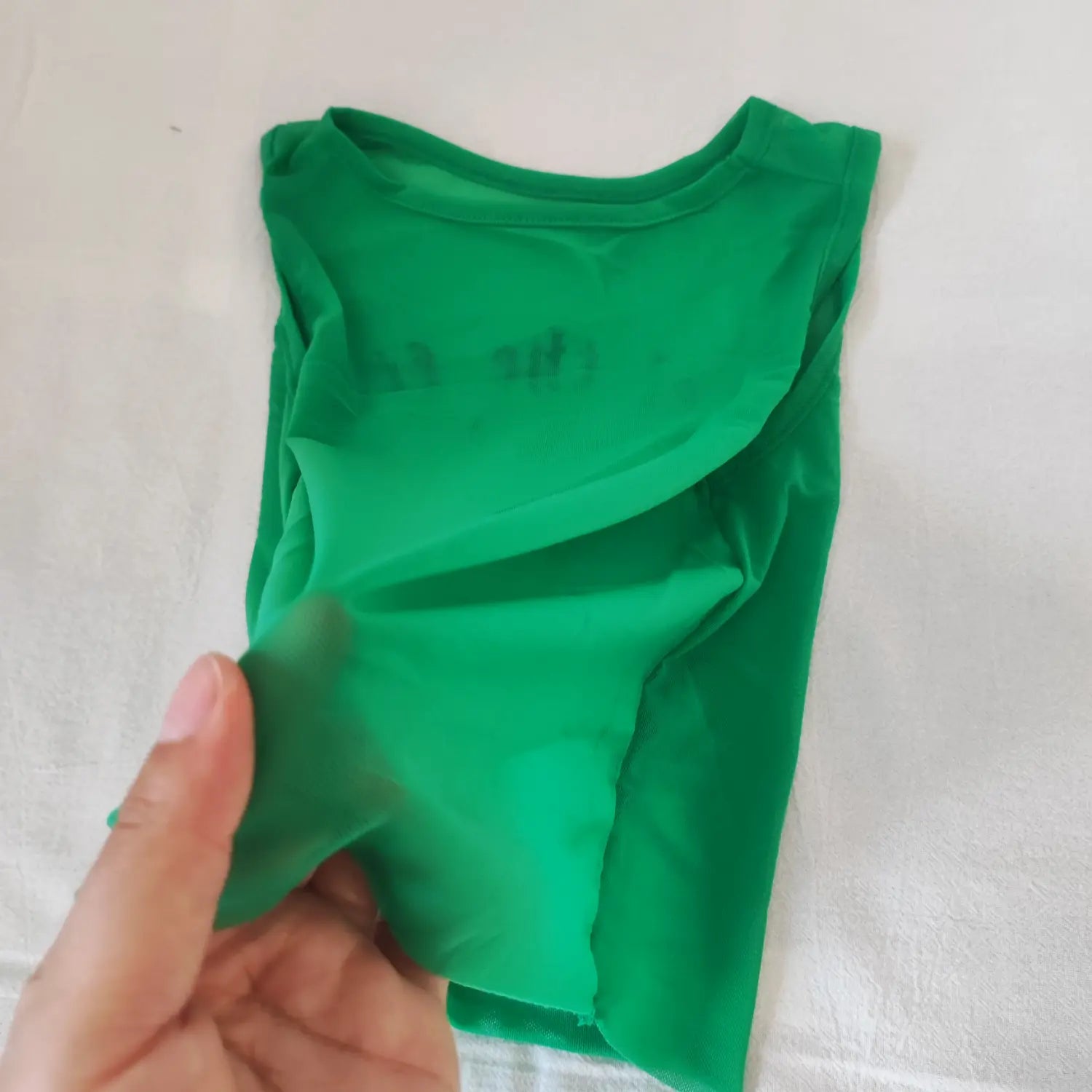 Close‑up hand stretching green sheer mesh fabric to show see‑through texture of cropped tank top
