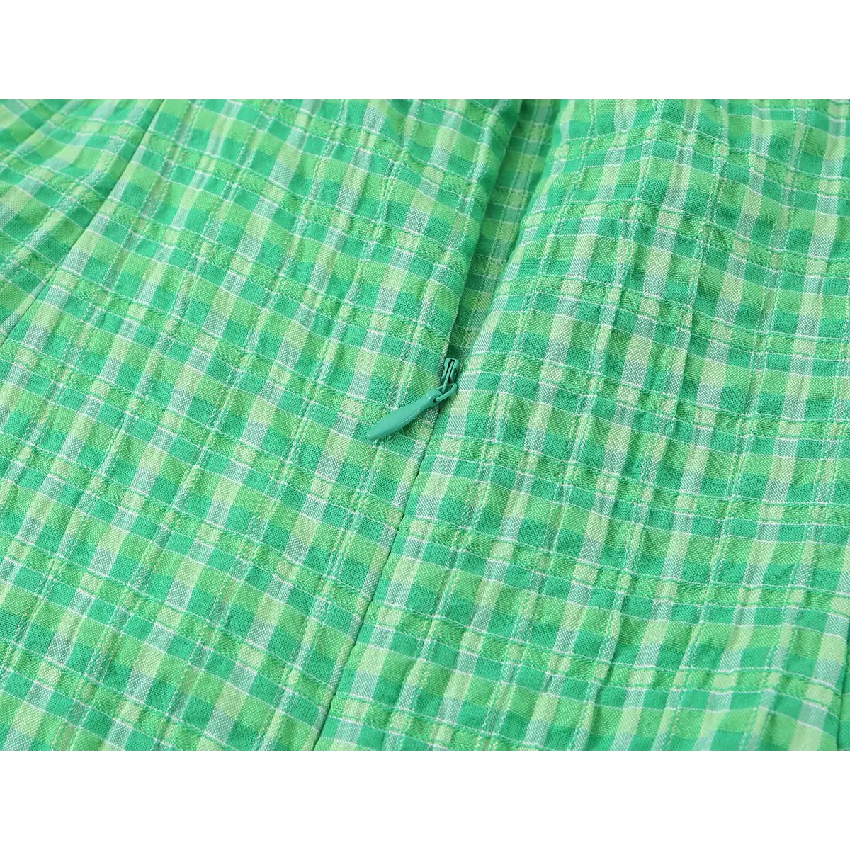 Close-up of the dress's side zipper, showing the green pull tab and how it blends with the gingham fabric.
