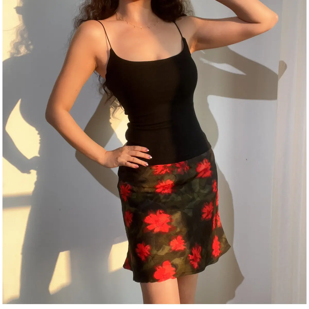 Woman wearing a green and red floral chiffon mini skirt, paired with a black ribbed camisole, showing the skirt's silhouette and print.