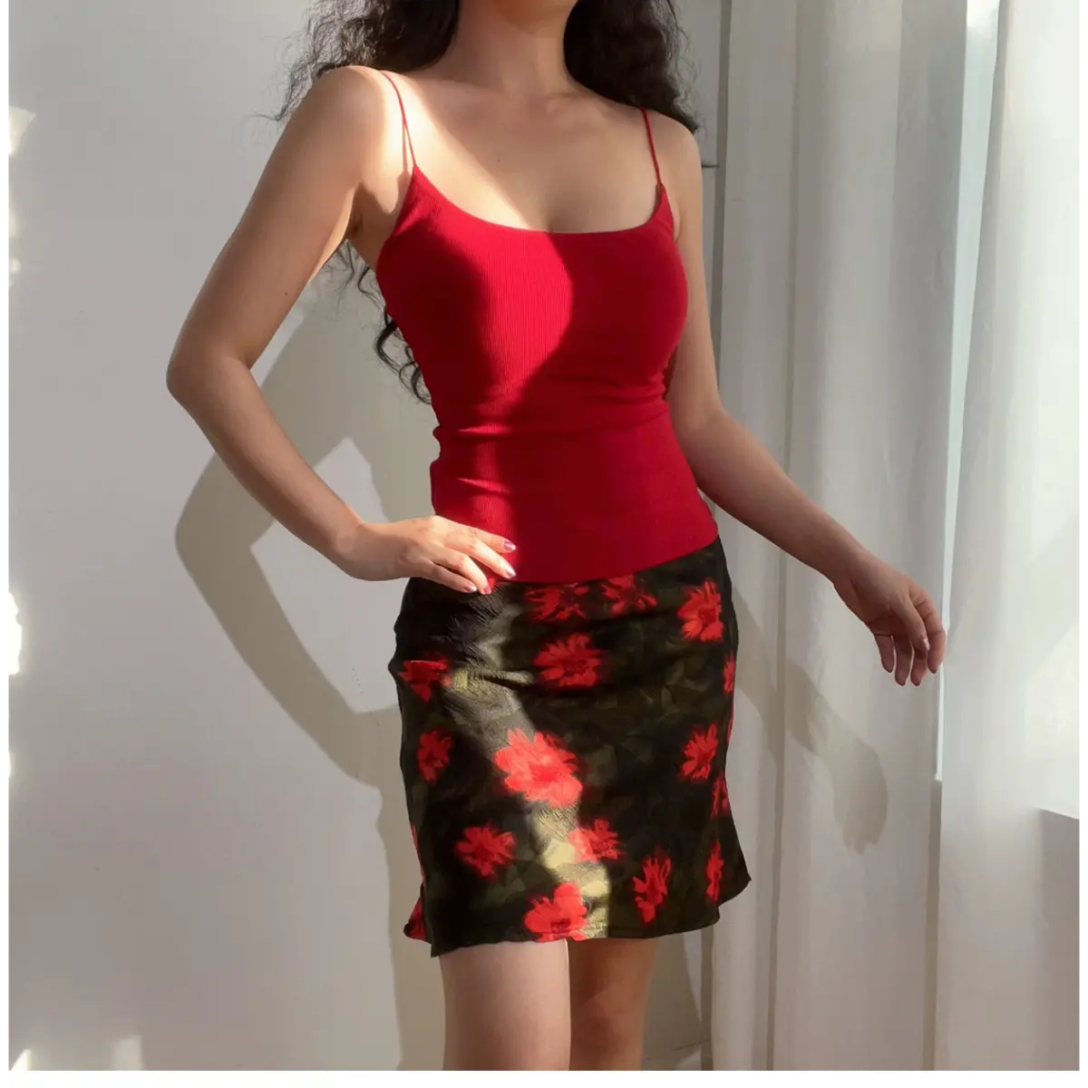 Angled view of a woman wearing a green and red floral chiffon mini skirt, paired with a red ribbed camisole, showing the print and flowy hem.