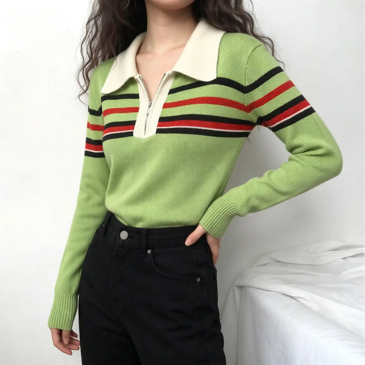 Model wearing green knit sweater with cream collar and stripe trim, paired with black high-waisted jeans