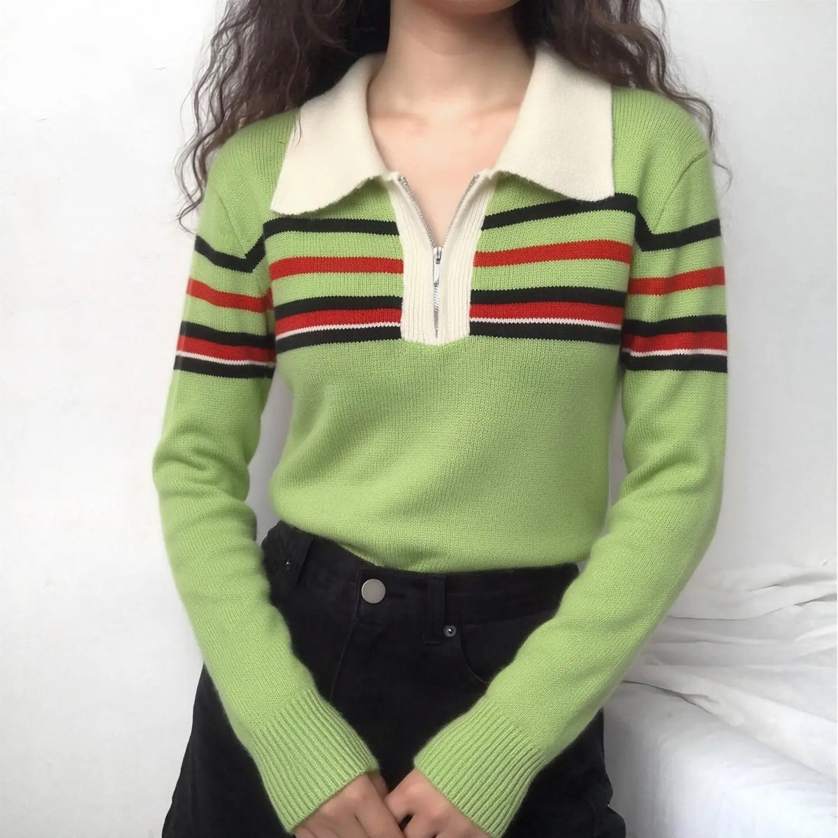 Model wearing green knit sweater with cream collar and black red white stripes, paired with black jeans