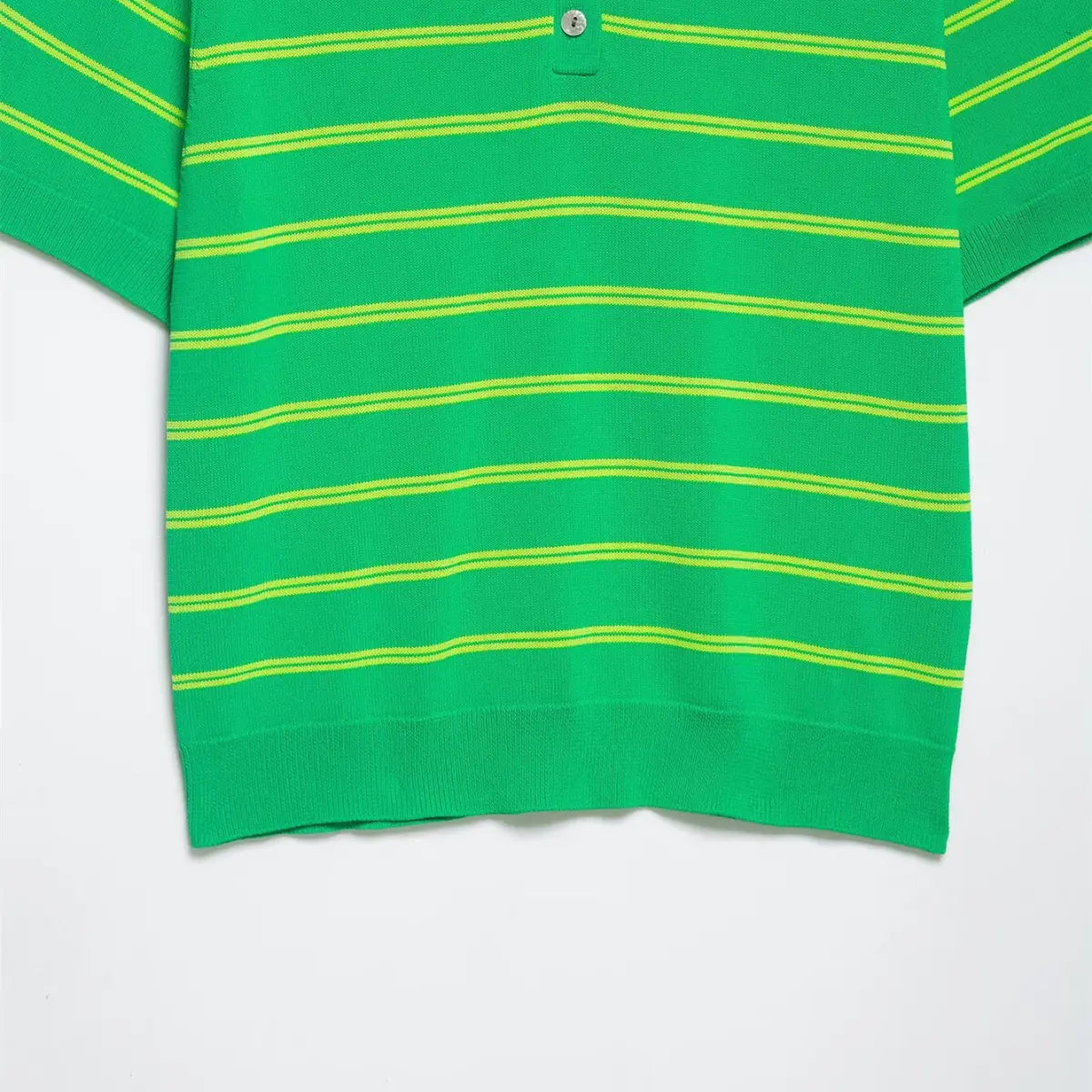  Close-up of the lower hem on the green and yellow striped knit polo shirt, showing the ribbed finish and mother-of-pearl button placket