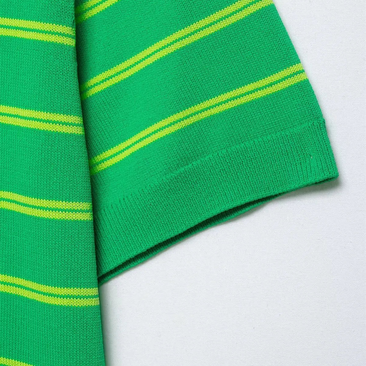 Close-up of the short sleeve cuff on the green and yellow striped knit polo shirt, showing the ribbed hem and stripe pattern