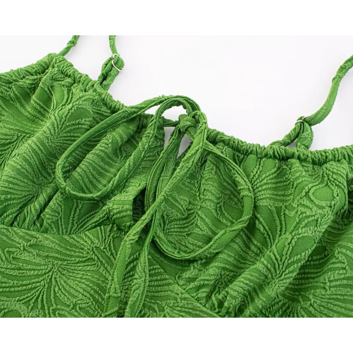 Close-up view of the bust area of a green textured mini dress with spaghetti straps, showing the front tie keyhole detail and embossed leaf pattern.