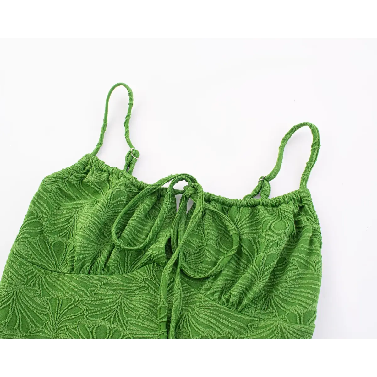 Macro view of the front tie keyhole detail on a green textured mini dress, highlighting the embossed leaf fabric pattern.