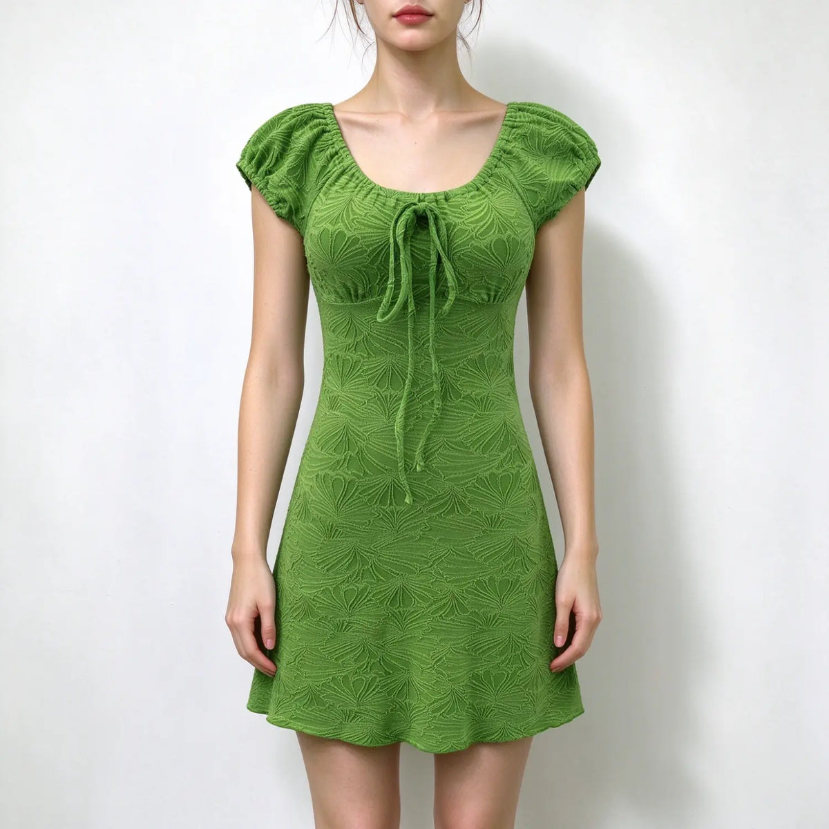 Model wearing green textured puff sleeve mini dress with square neck and front tie detail, plain white background